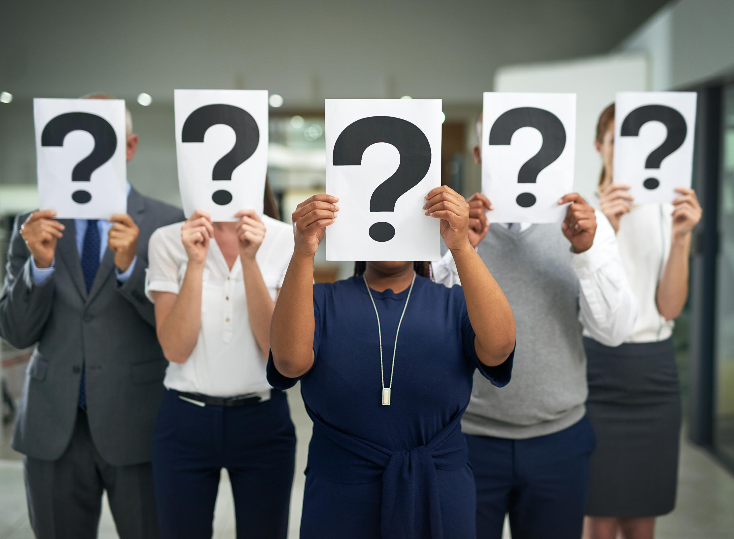 Shot of a group of businesspeople holding questions marks in front of their faces.